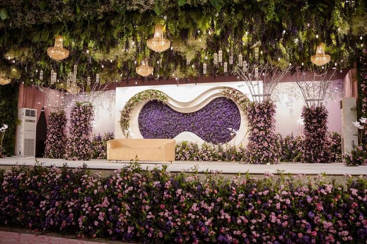 Purple and white floral stage with a wave-form centrepiece and hanging greenery by RAW Group